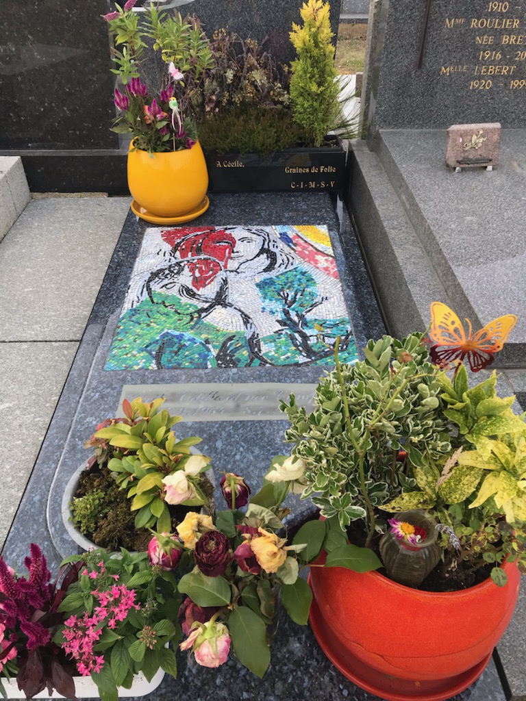 Pierre tombale avec au premier plan des fleurs, puis une mosaïque colorée et des fleurs