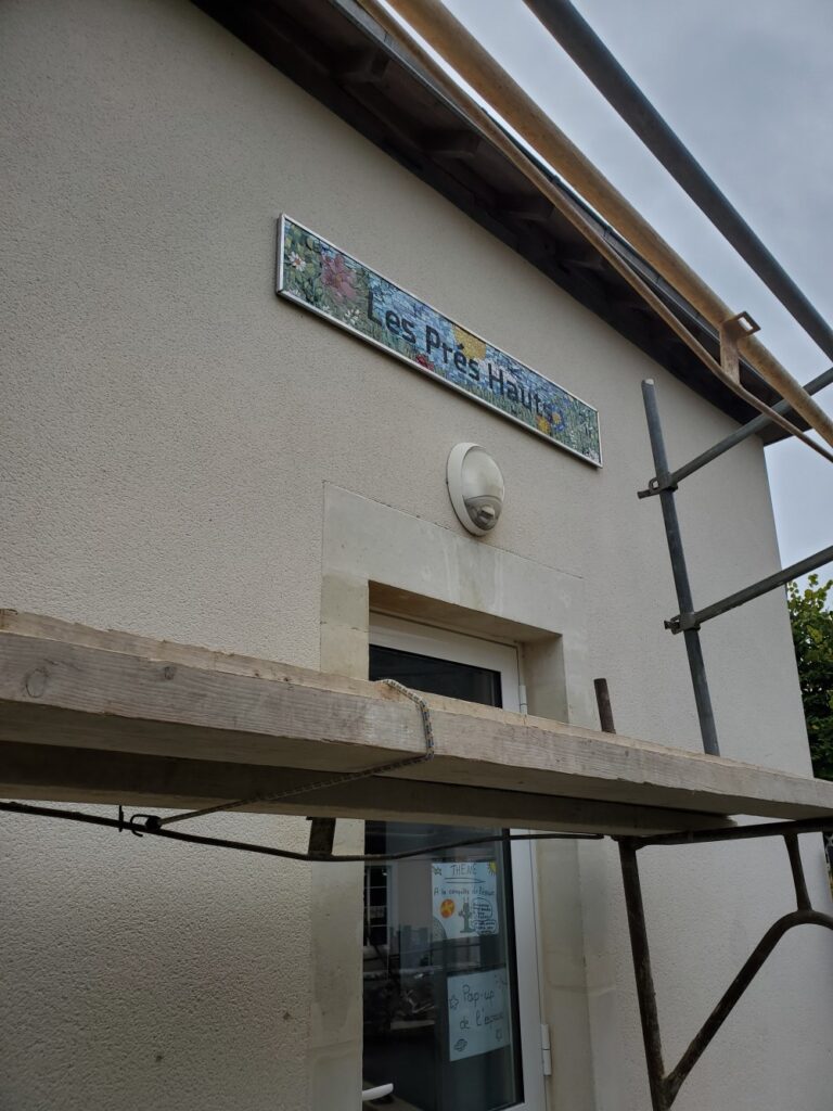 vue de l'échafaudage devant le mur de l'école où la fresque en mosaïque avec le nom Les prés hauts a été posée