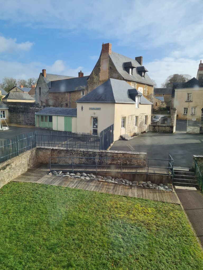 paysage de l'école des Prés hauts avec de l'herbe au premier plan, ensuite une partie de la cour et le bâtiment sur lequel est posée la fresque en mosaïque réalisée par les élèves avec la supervision de Céline Loury