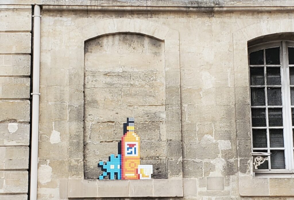 Sur cette image, il y a une partie d'un personnage Space Invader caché derrière une bouteille de pastis 51, cette photo a été prise à Marseille en 2024