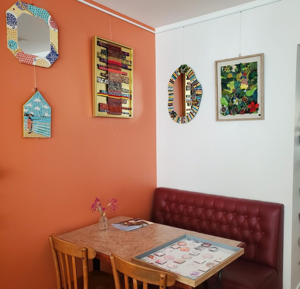lieu salon de thé où il y a un mur de couleur Terra cotta avec des oeuvres en mosaïque de Céline Loury, deux miroirs colorés, une oeuvre en plaque de verre taillée, une mosaïque d'une pecheuse à cancale