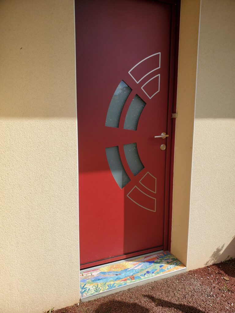 photo de la porte d'entrée rouge avec le seuil de porte en mosaïque par Céline Loury