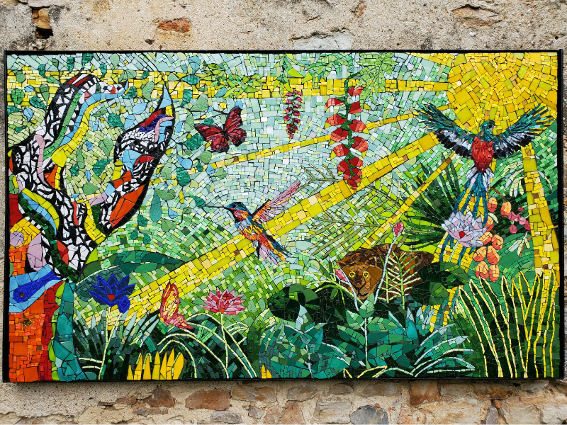 Mosaïque représentant une ambiance tropicale avec à gauche, l'arbre de Niki de Saint Phalle, le colibri, un Quetzal, Le Douanier Rousseaue t les rayons du soleil. Une réalisation à quatre mains par Céline Loury et Fanny Guillo